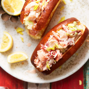 Two lobster rolls on a plate with lemon wedges