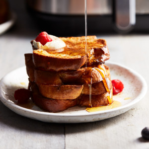 Pouring maple syrup over a stack of freshly cooked French toast