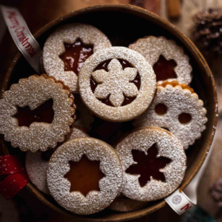 a dozen filled Linzer cookies in a wooden basket with powdered sugar on top