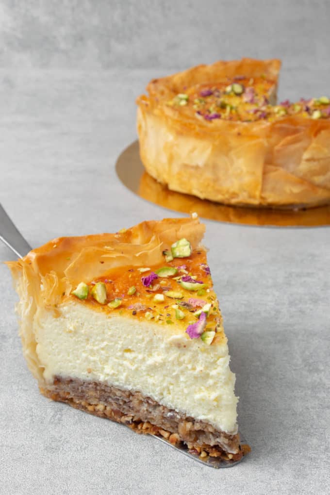 A piece of Baklava cheesecake on a grey background topped with pistachio crumbles