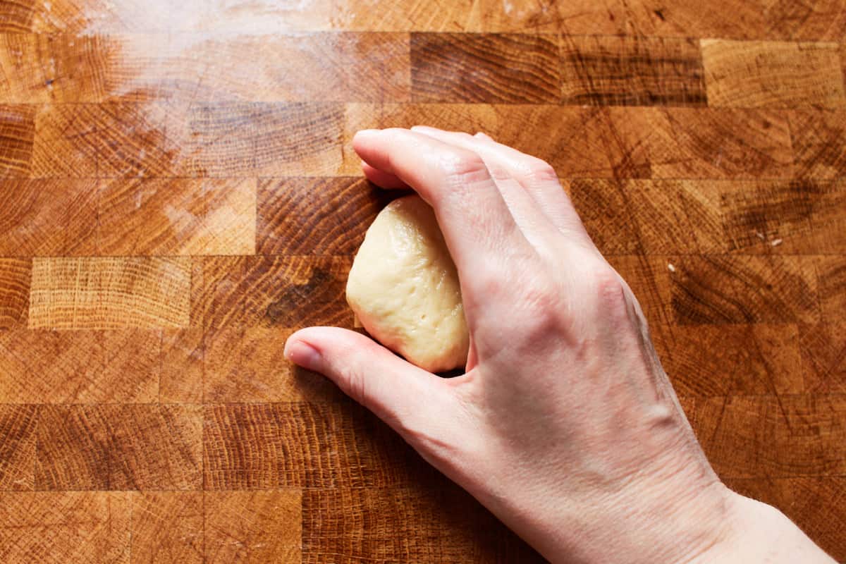 Making a c shape with a hand that is cupping a piece of dough