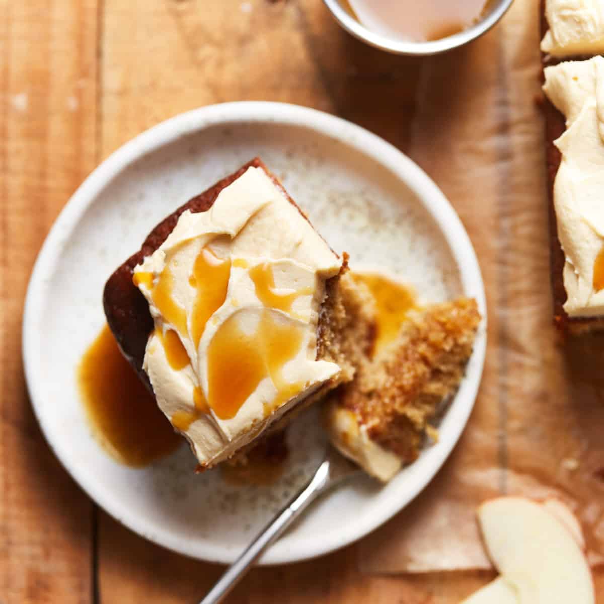 A slice of frosted apple cake with caramel syrup on a plate with a bite missing