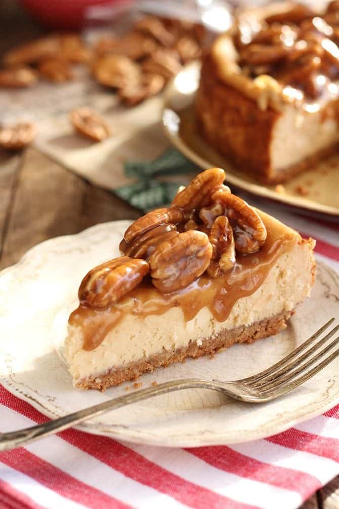 a slice of cheesecake on a white plate topped with pecans and caramel sauce