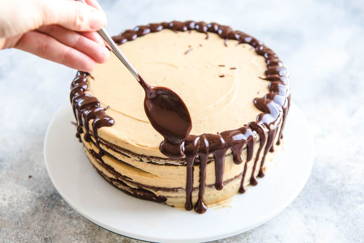 Spooning chocolate ganache over the sides of a cake