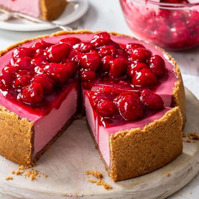 pink colored cheesecake where one third is missing topped with raspberries on a white platter