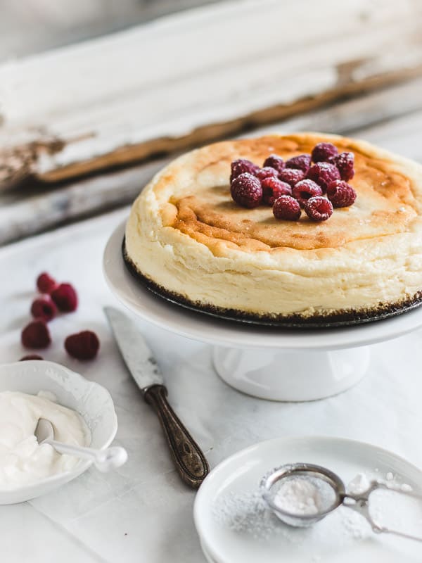 a whole cheesecake decorated with sugared raspberries on a white cake stand