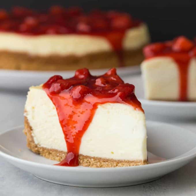 a slice of cheesecake on a dessert plate with strawberry sauce on top