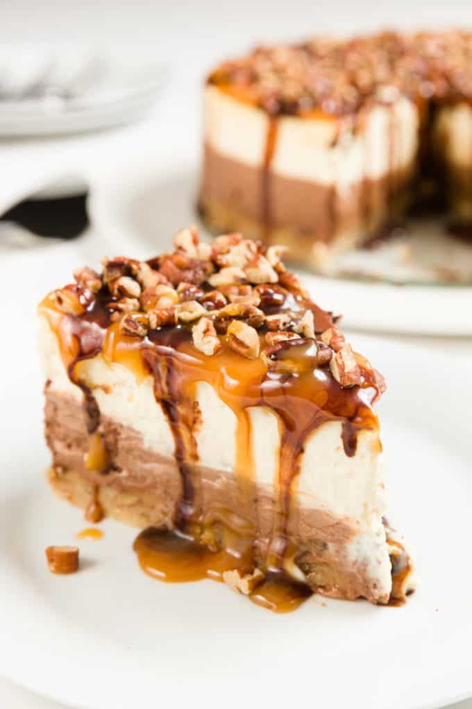 a piece of turtle cheesecake topped with pecans and caramel on a white plate