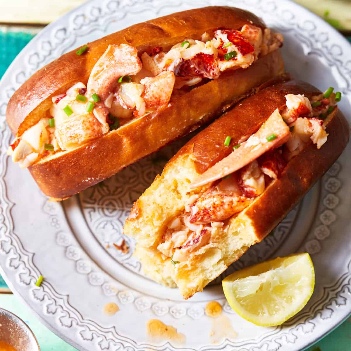 Two lobster sandwiches on a plate with one being half eaten