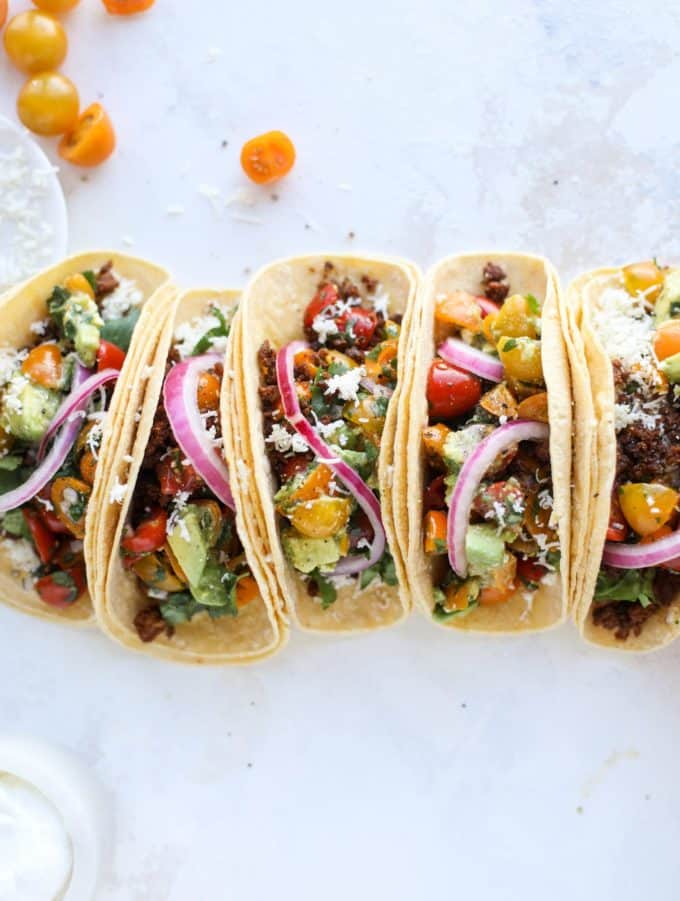 Five beef tacos on a white table