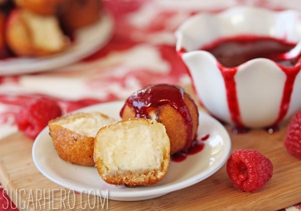 two fried cheesecake balls one cut in half with berry sauce on a white plate