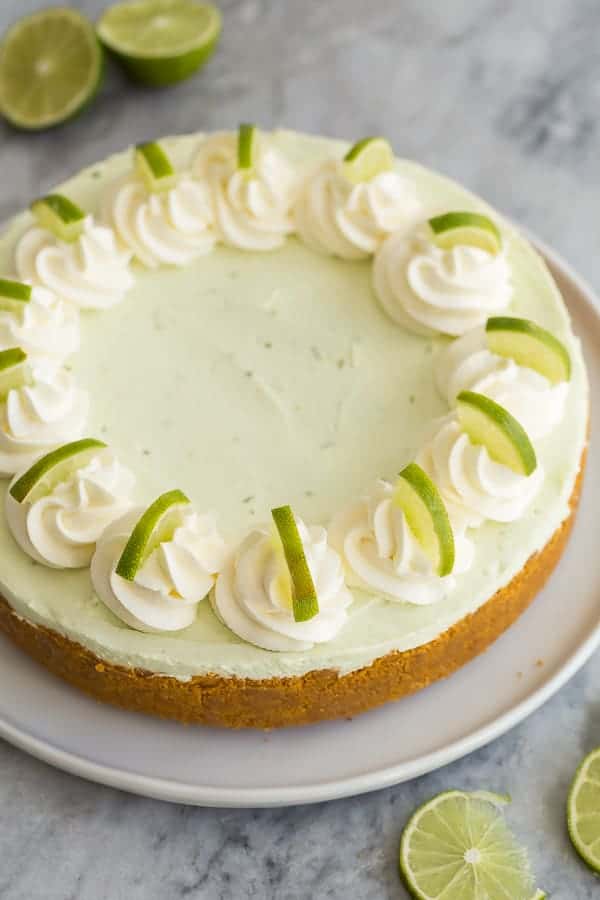 a whole cheesecake decorated with whipped cream and lime slices on a white plate
