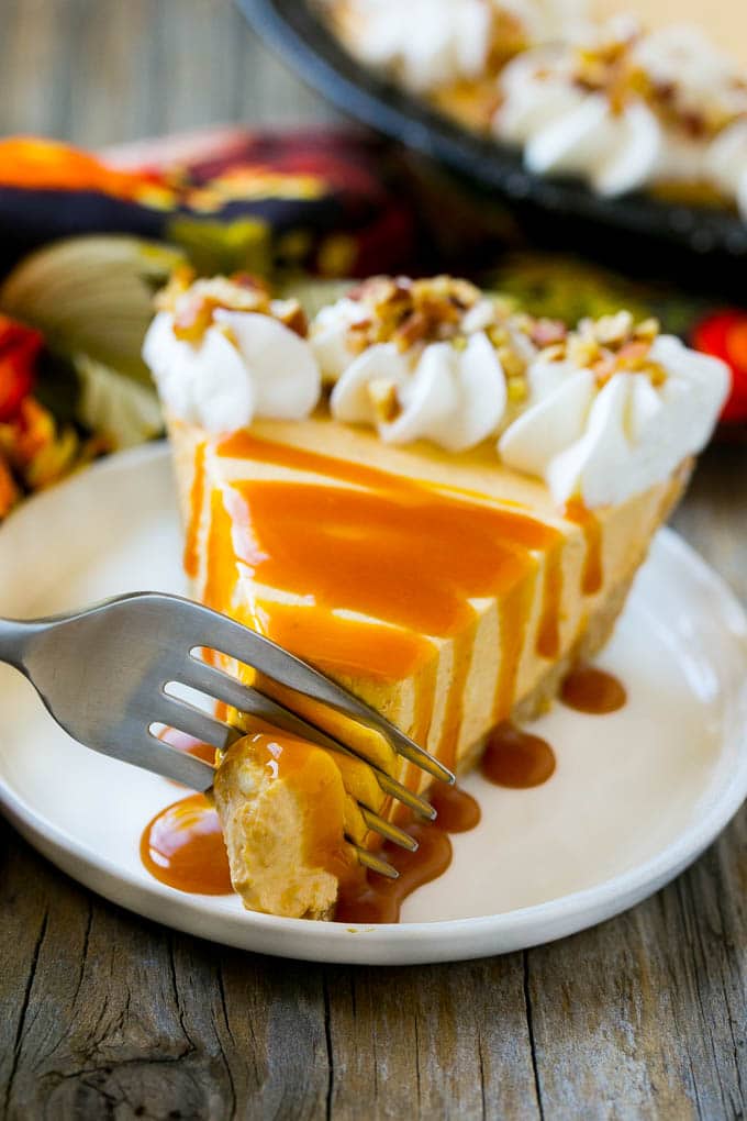 a piece of pumpkin cheesecake with whipped cream and caramel sauce on a white plate with a fork