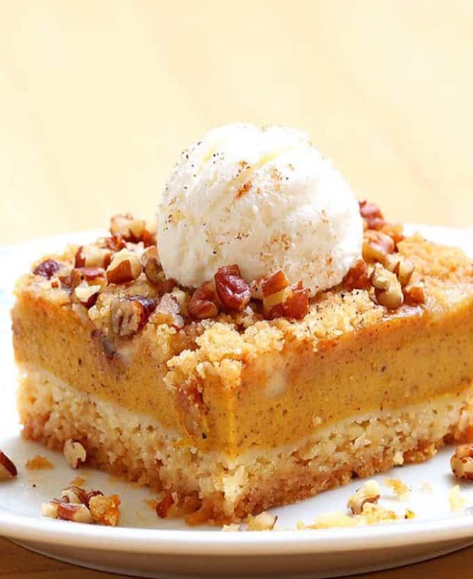 Two layered pumpkin dessert slice topped with ice cream and pecans