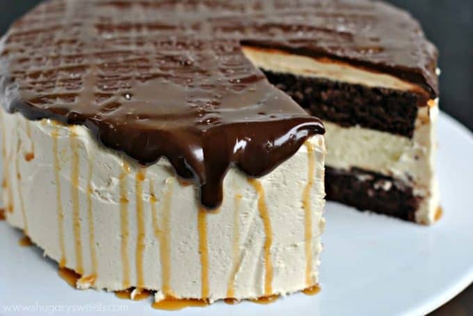 a whole cake topped with chocolate ganache and caramel sauce where one slice is missing on a white plate
