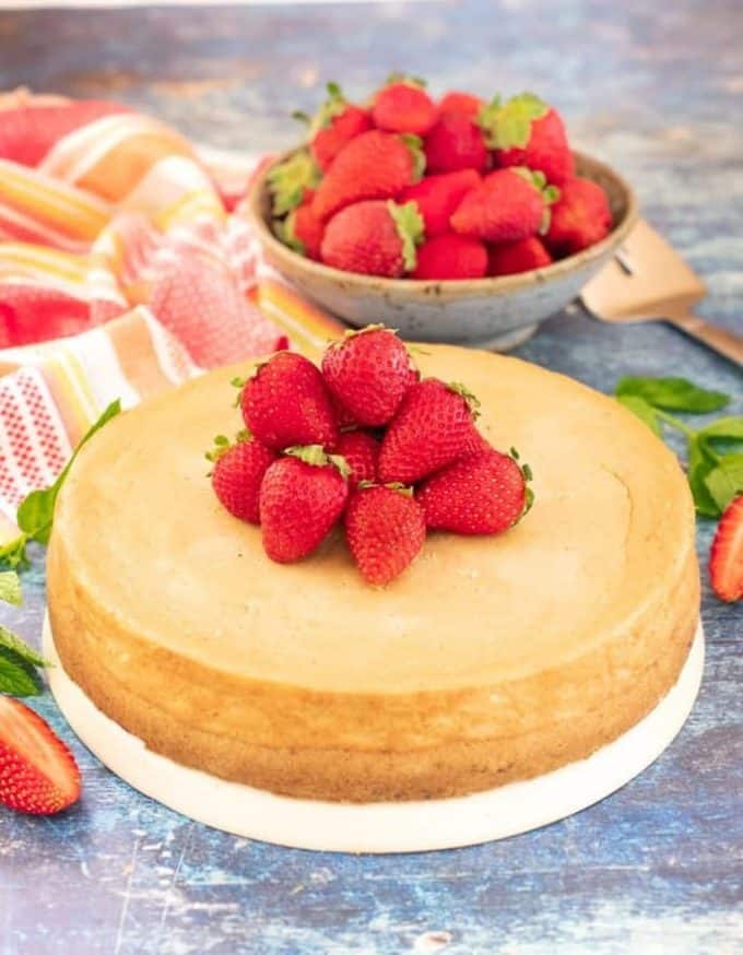 a whole new york cheesecake on a white plate decorated with strawberries