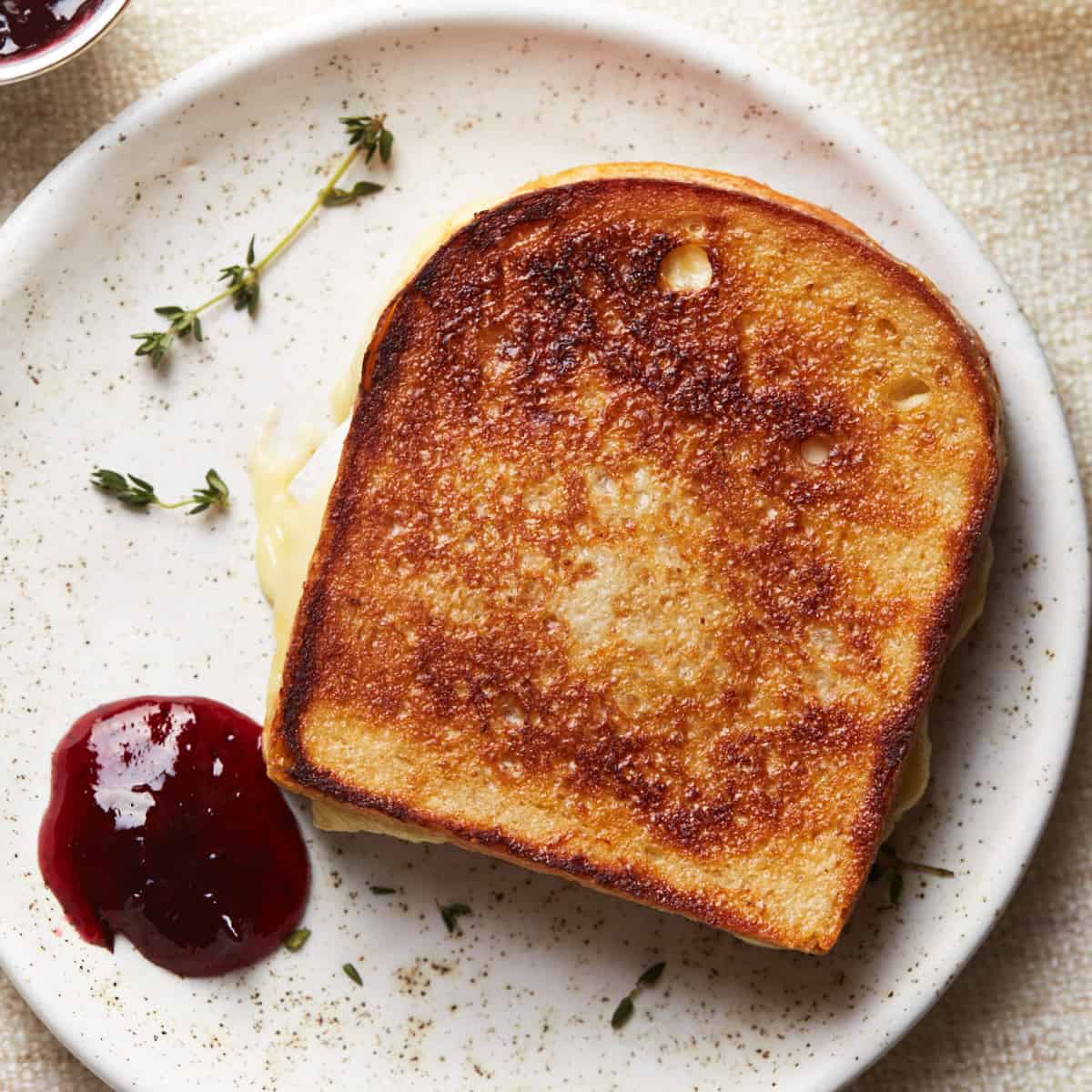 Grilled cheese sandwich with cranberry sauce and thyme on a dinner plate