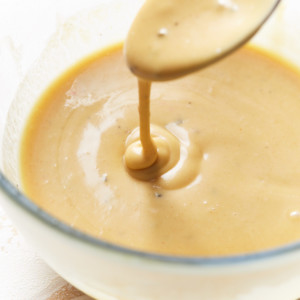 A bowl full of honey mustard sauce with sauce dripping down a spoon into the bowl