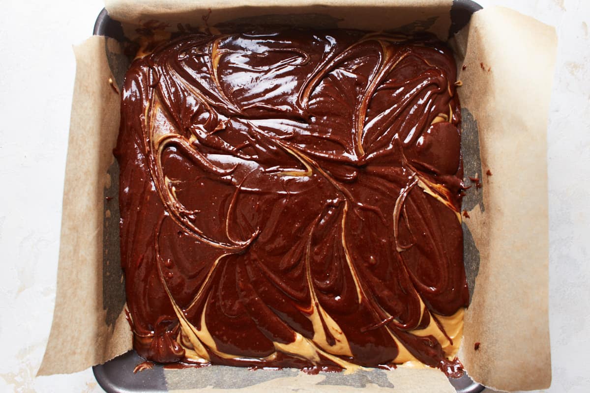 Unbaked brownie batter in a pan with a peanut butter swirl