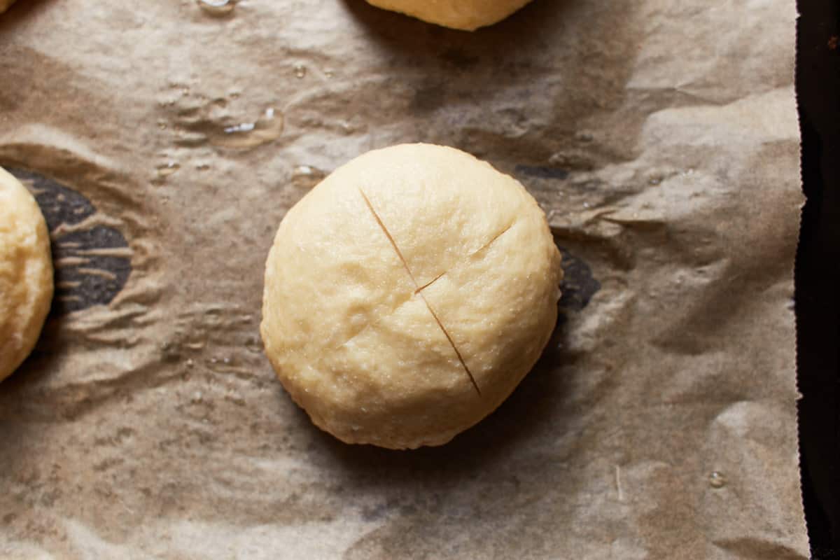 A cooked ball of dough on a baking sheet with a large x cut across the surface