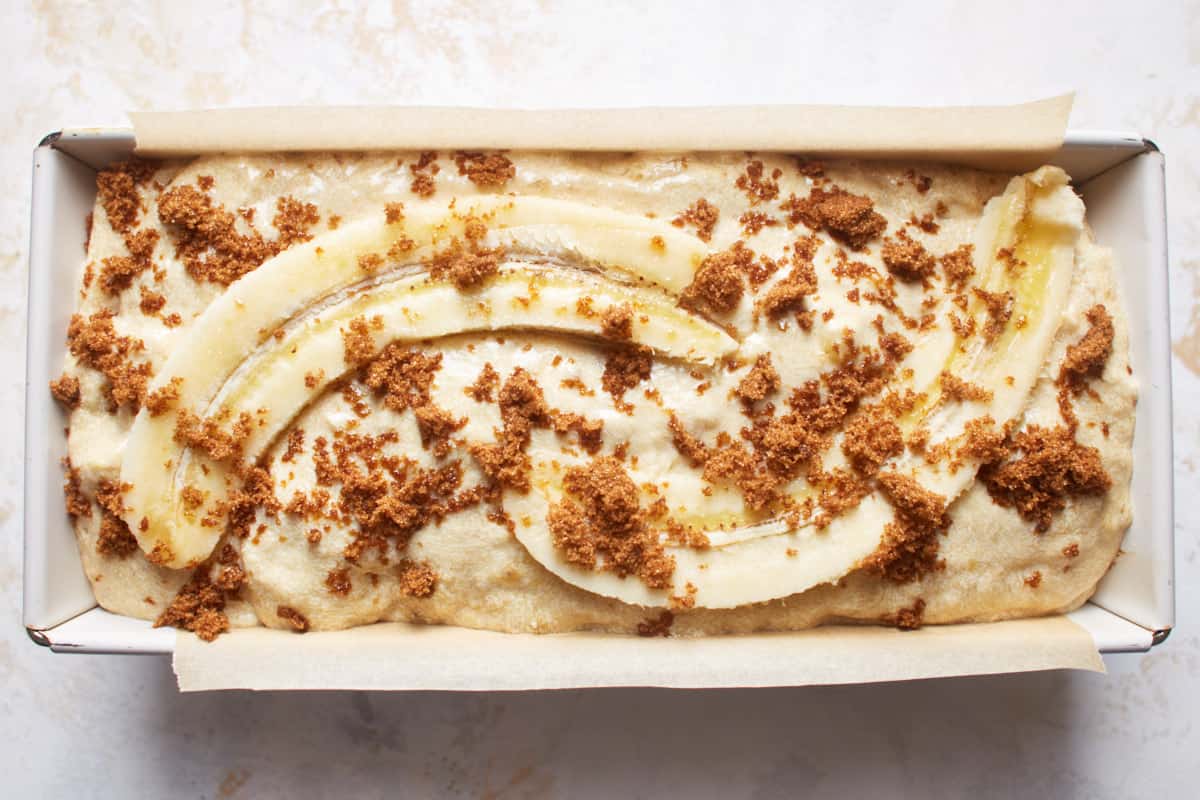 Banana bread batter in a loaf pan sprinkled with sugar and topped with a halved banana