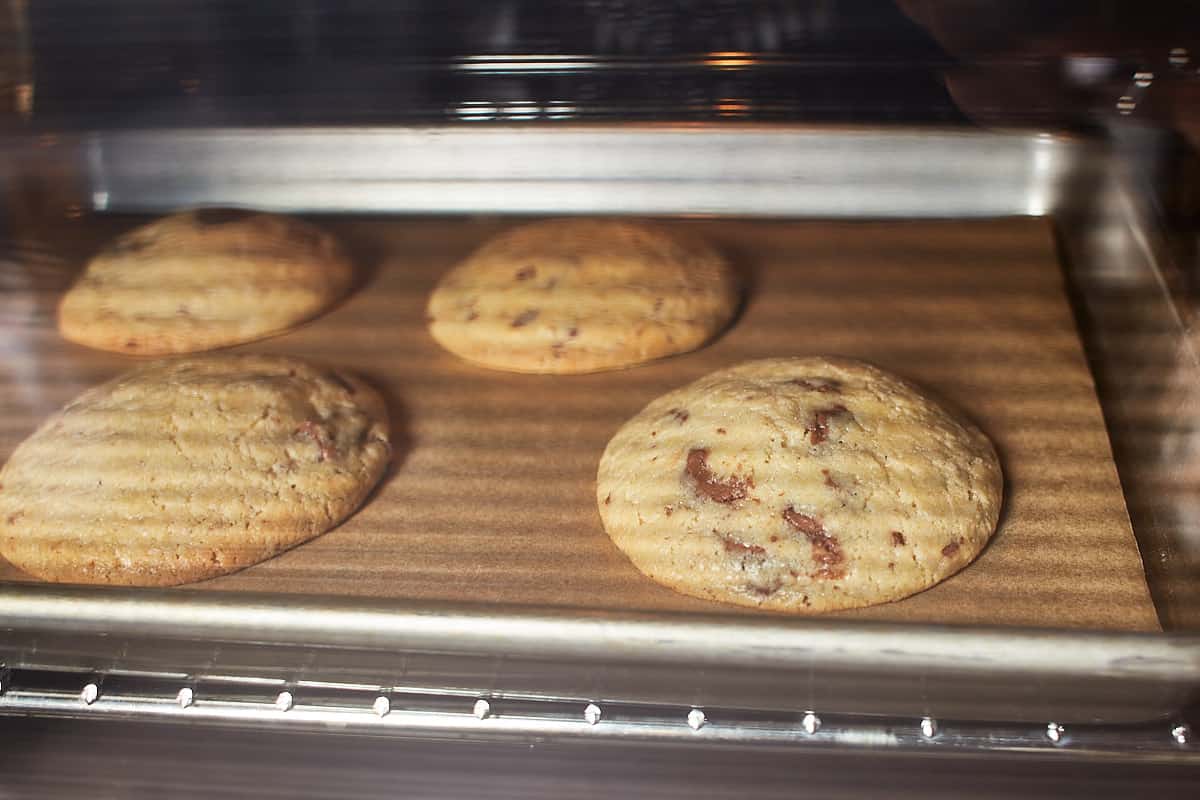 Four cookies on a baking sheet baking in the oven