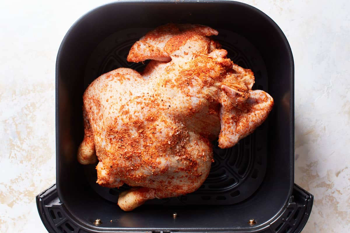 Uncooked whole chicken arranged breast side down in an air fryer basket