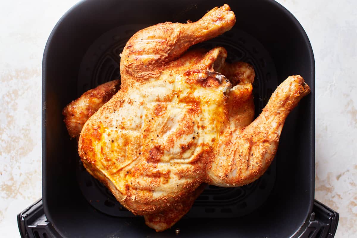 Half cooked whole chicken arranged breast side up in an air fryer basket