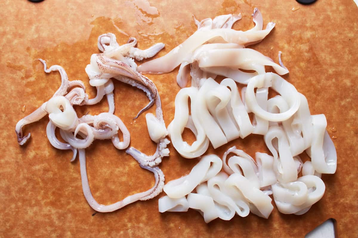 Whole squid cut into rings and tentacles on a wooden cutting board
