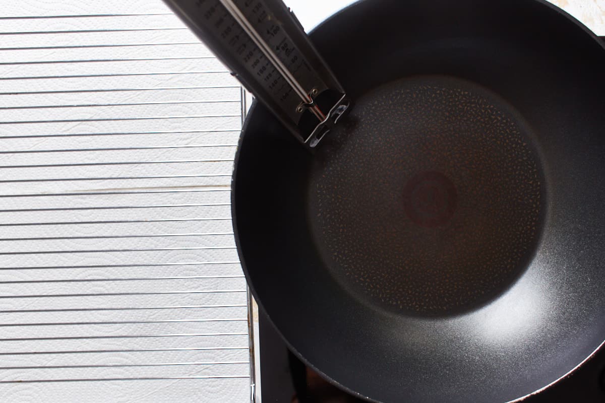 Wok placed on a burner with a thermometer inside and a wire rack next to it