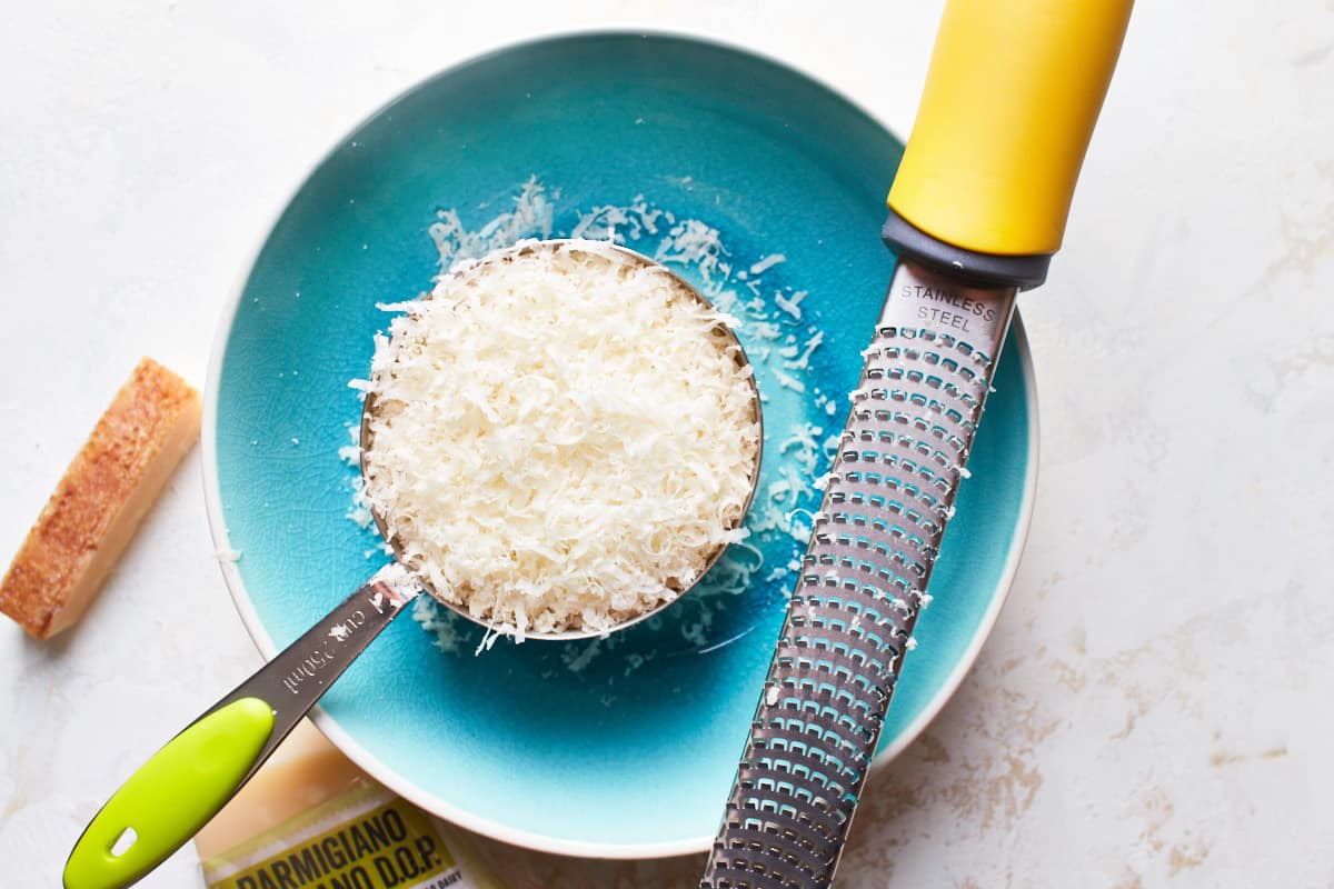 Grated parmesan cheese in a measuring cup on a plate and a grater