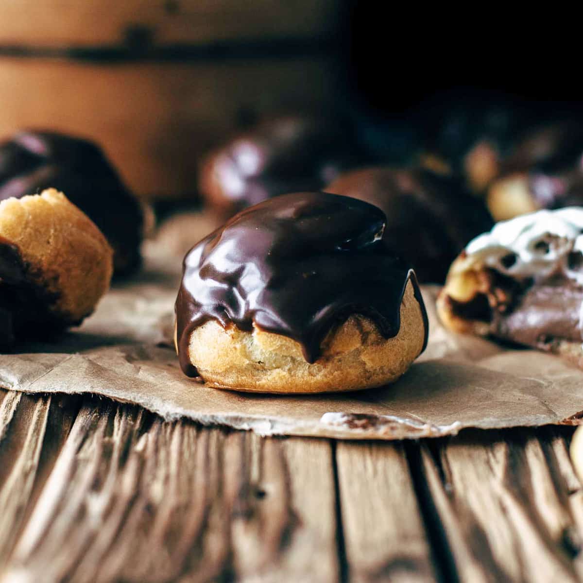Glazed and filled chocolate cream puffs on a brown table