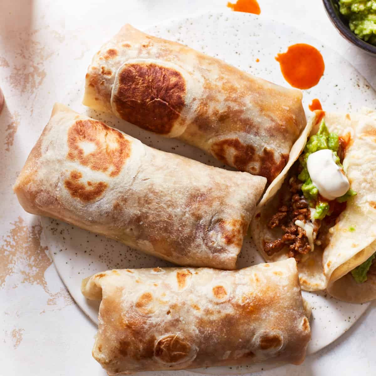 Three burritos and one soft taco filled with beef on a serving plat