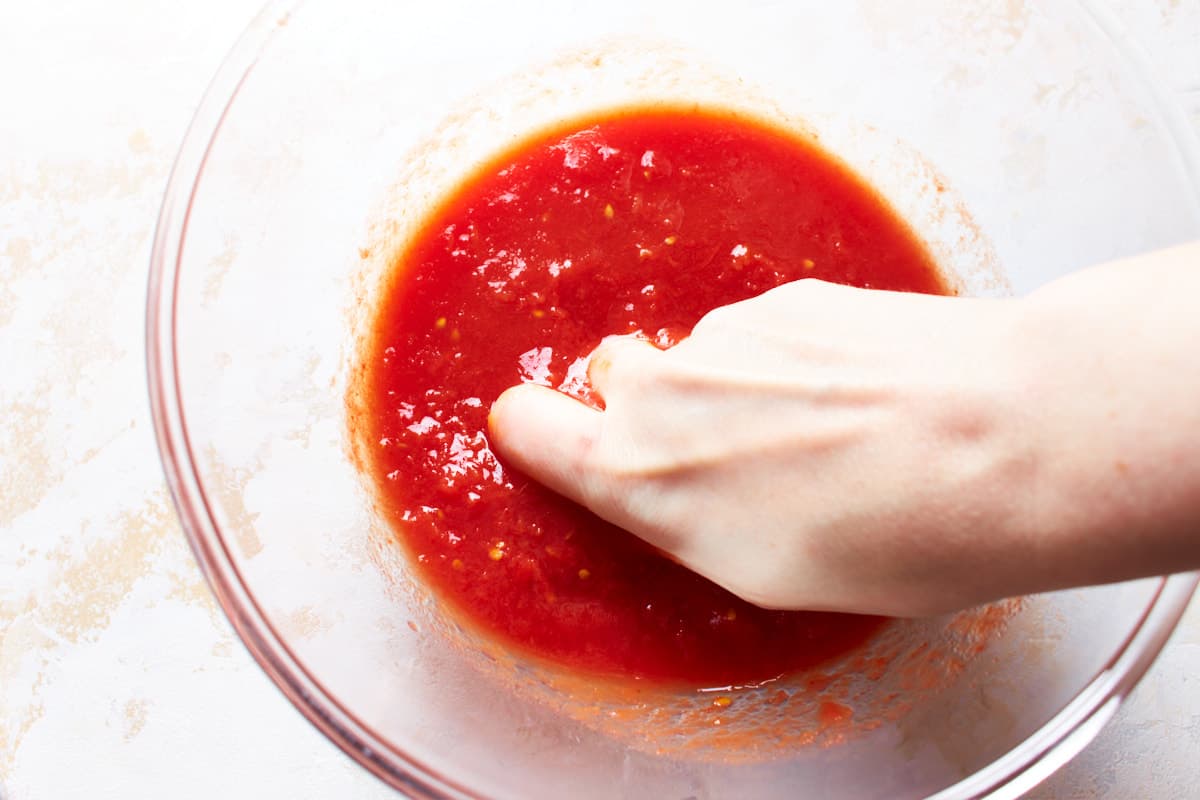 Crushing canned tomatoes with a hand