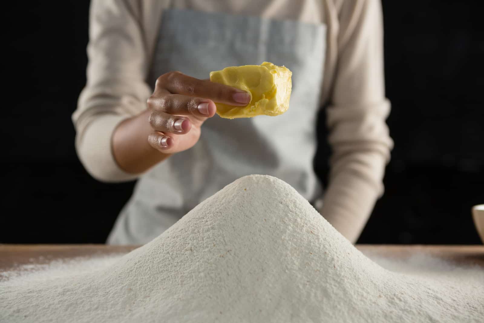 a woman adding butter cube into flour