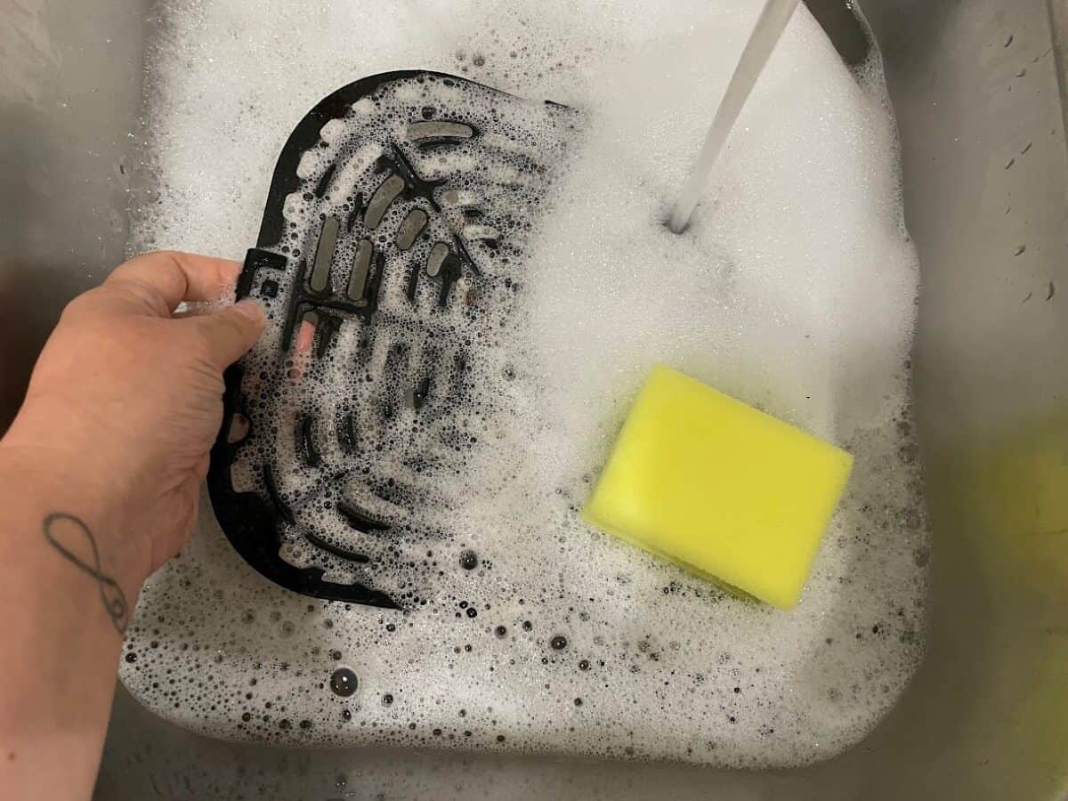 air fryer basket in sink with soapy water and sponge