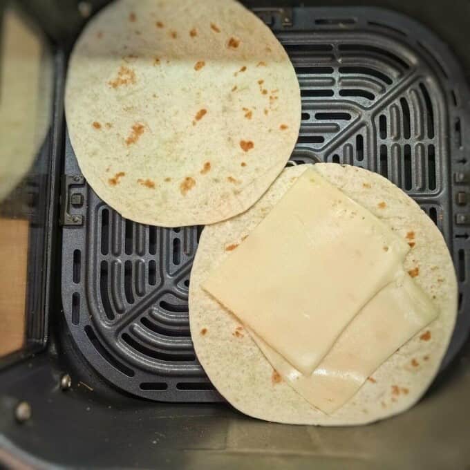 2 tortillas with slices of cheese in air fryer basket