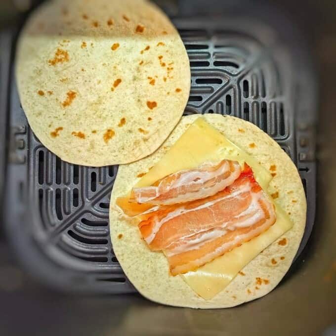 2 tortillas with slices of cheese and bacon in air fryer basket