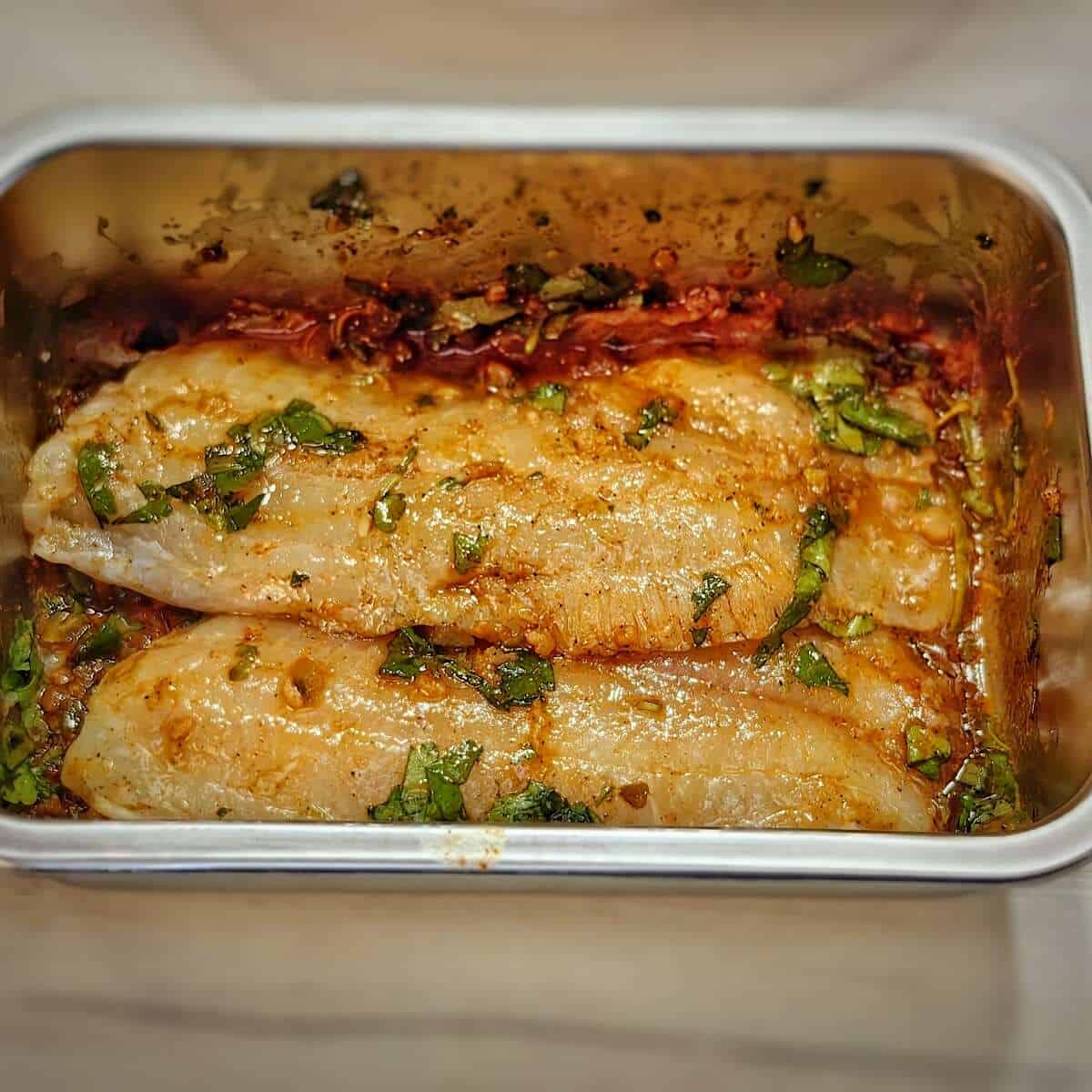 tilapia fillets with marinade in a metal container