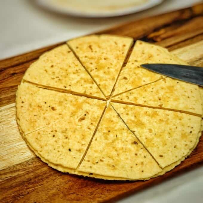 sliced corn tortilla on top of of a chopping board with knife