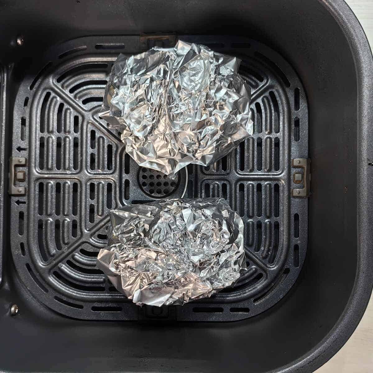 potatoes wrapped in foil inside air fryer basket