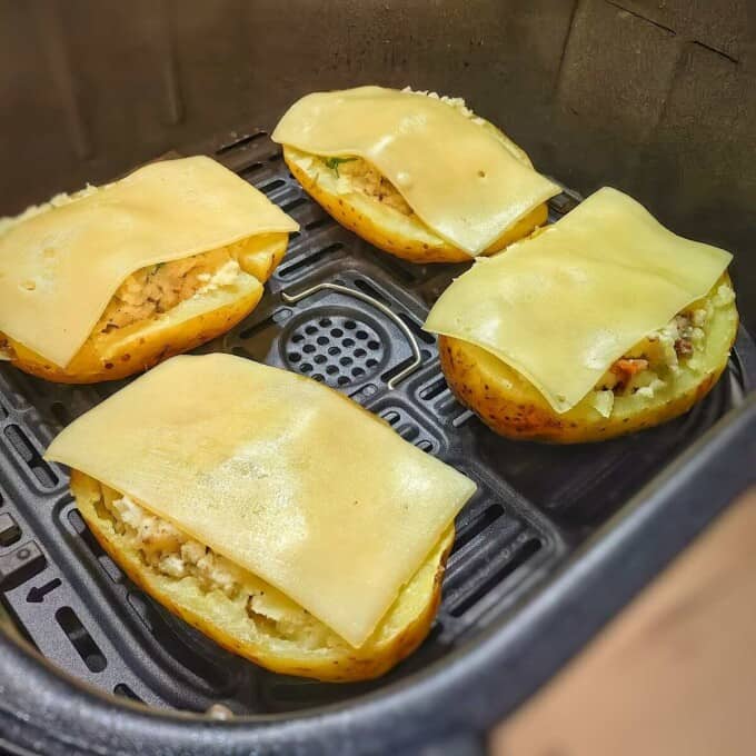 potato halves with filling mixture and cheese on top inside air fryer basket