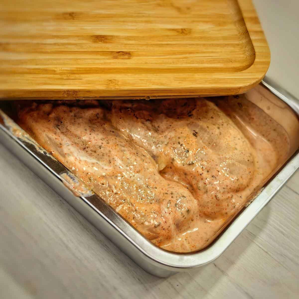 chicken marinating in a metal container with wooden lid
