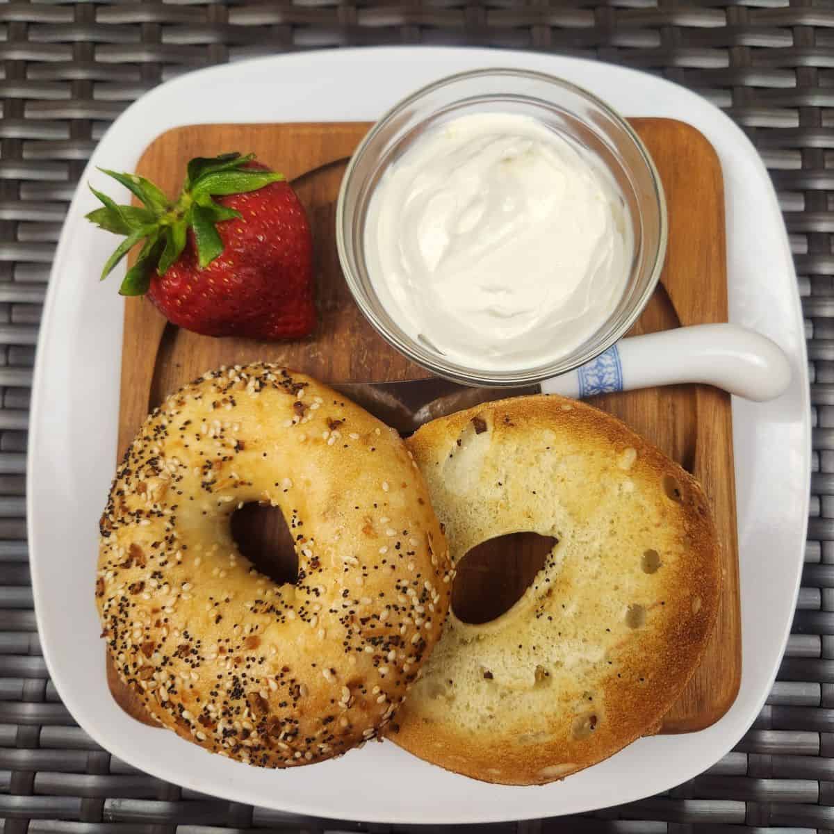 toasted bagel on a plate with white spread and strawberry