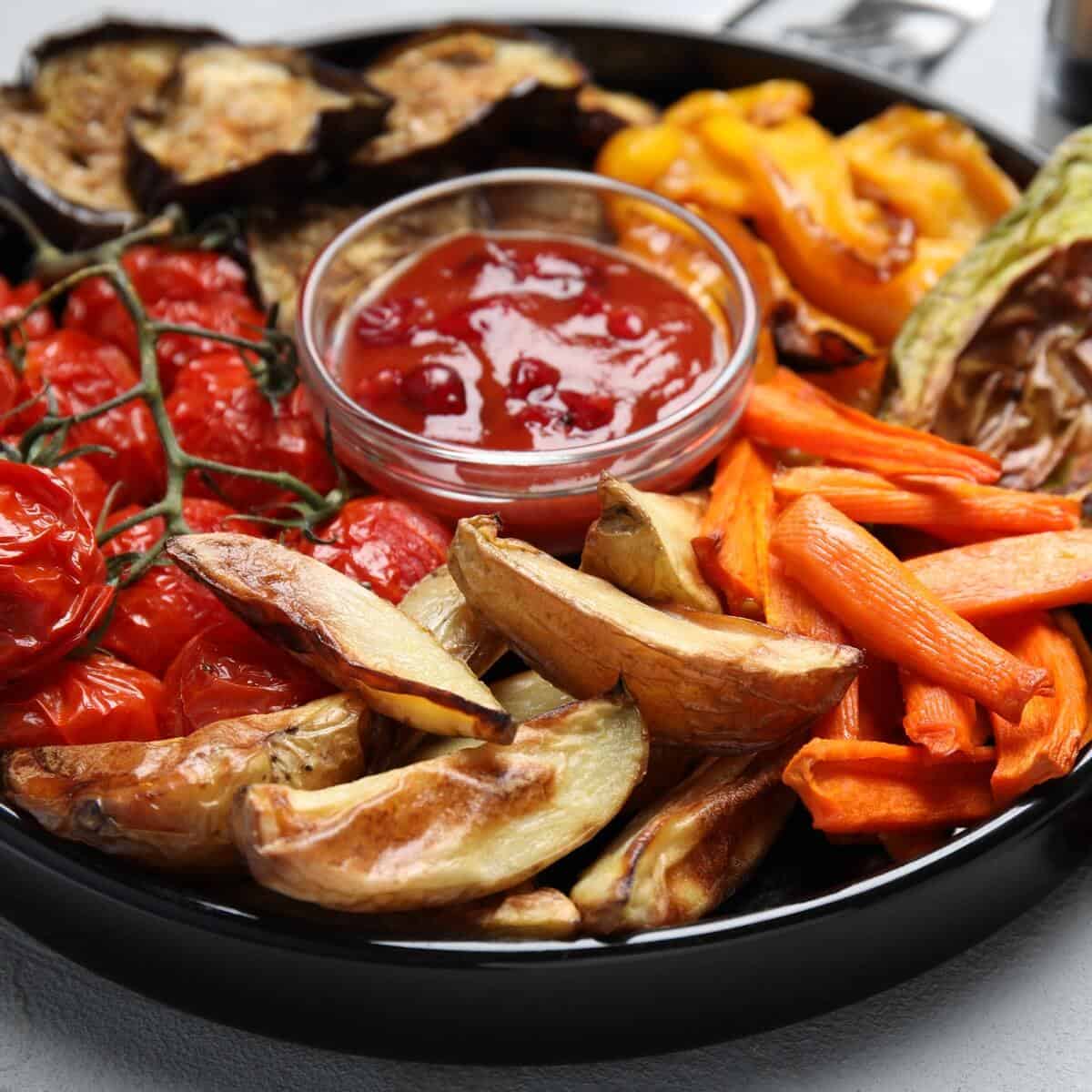 roasted vegetables on a black platter with red sauce