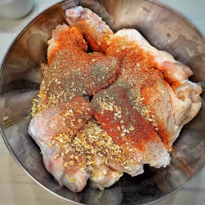 raw chicken wings with herbs and spices in a metal mixing bowl