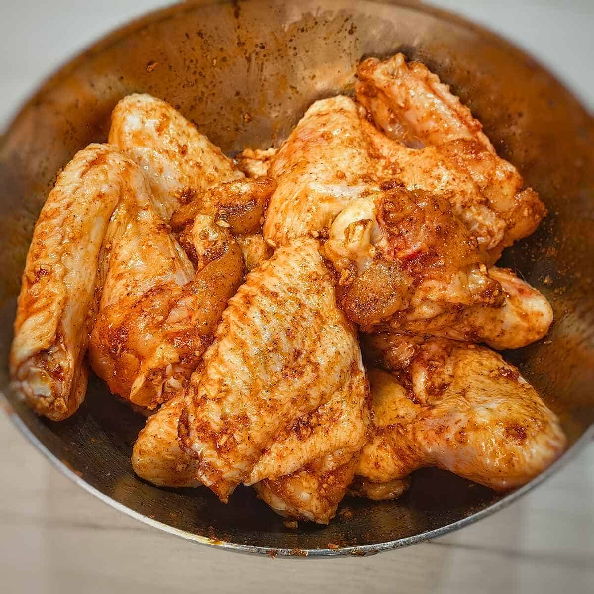 chicken wings coated with herbs and spices in a mixing bowl