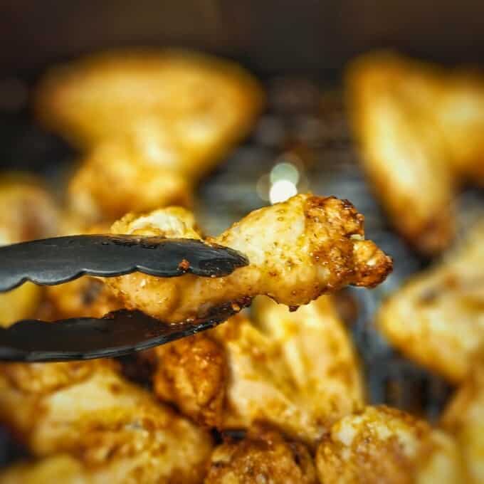 air fried chicken wings in kitchen tongs