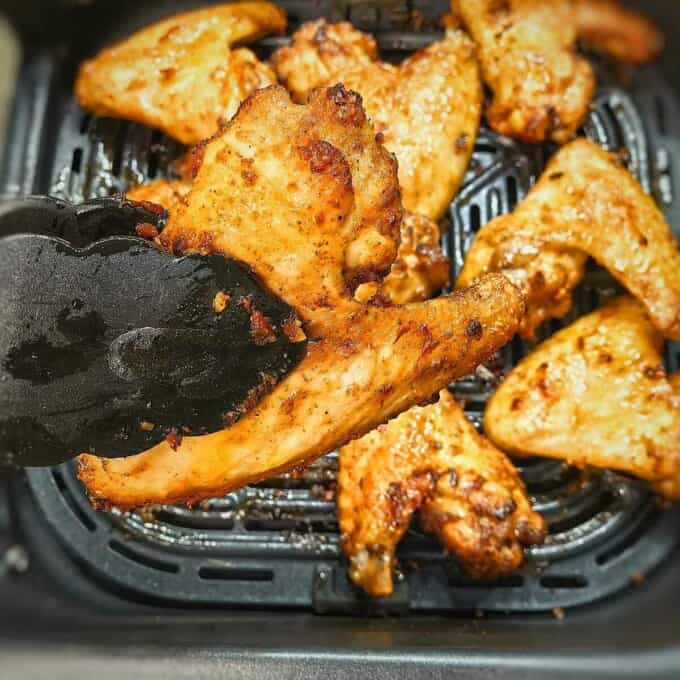seasoned chicken wings in kitchen tongs