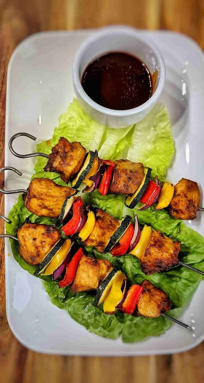 air fried chicken kabobs on a serving plate with bed of lettuce and dipping sauce